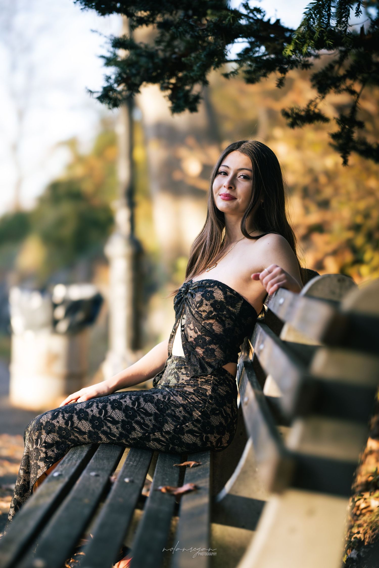 Woman in black lace dress posing gracefully on a park bench during golden hour.