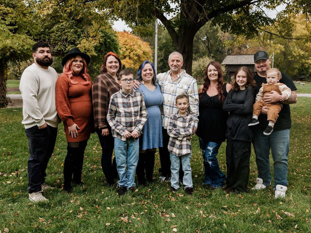 Large group gathering outdoors in casual attire with autumn trees in background.