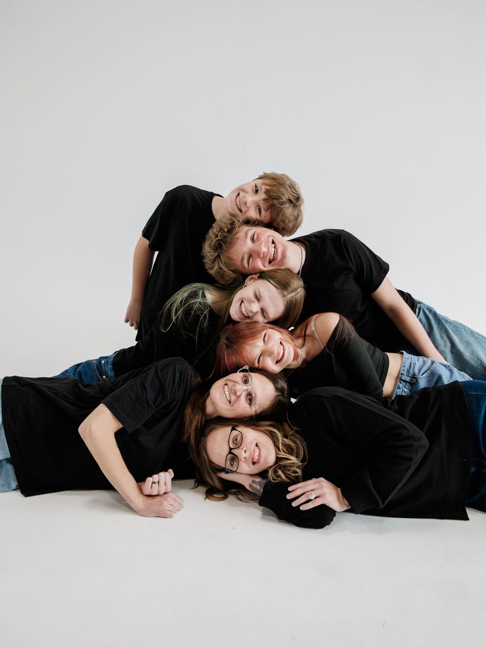 Studio portrait series of people lying down in black outfits against white background.