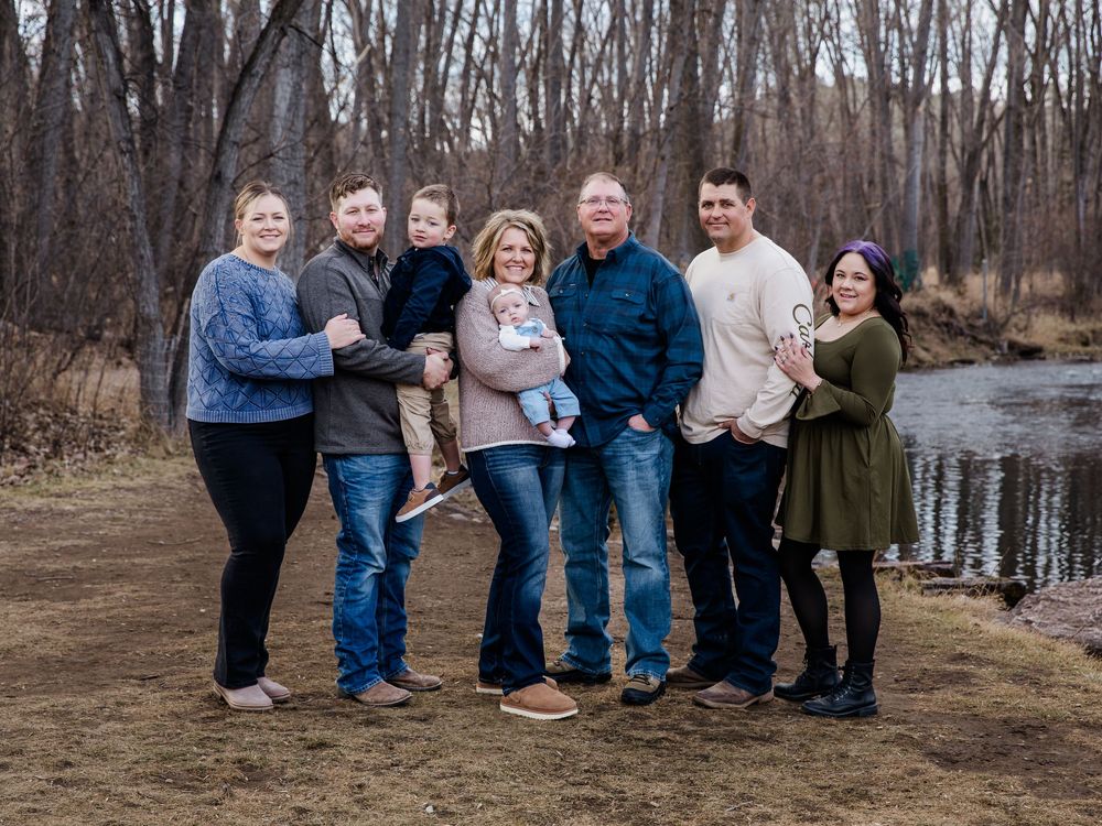 Family group photo session in casual wear against bare winter trees and natural backdrop.