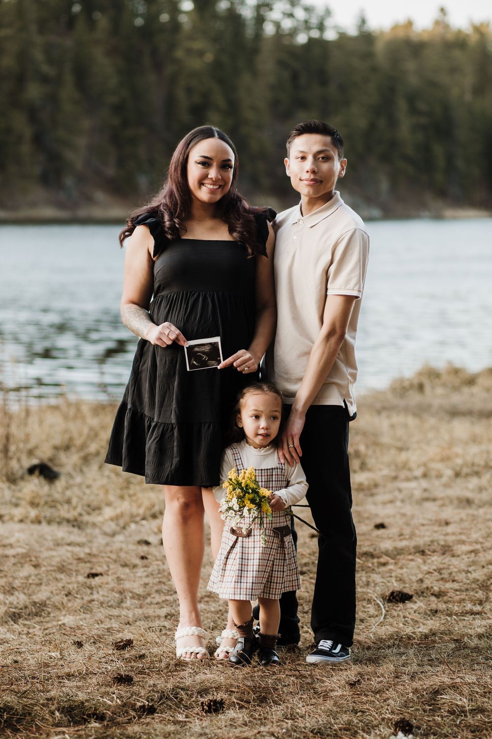 Family posing together by a lake with mountains in the background.