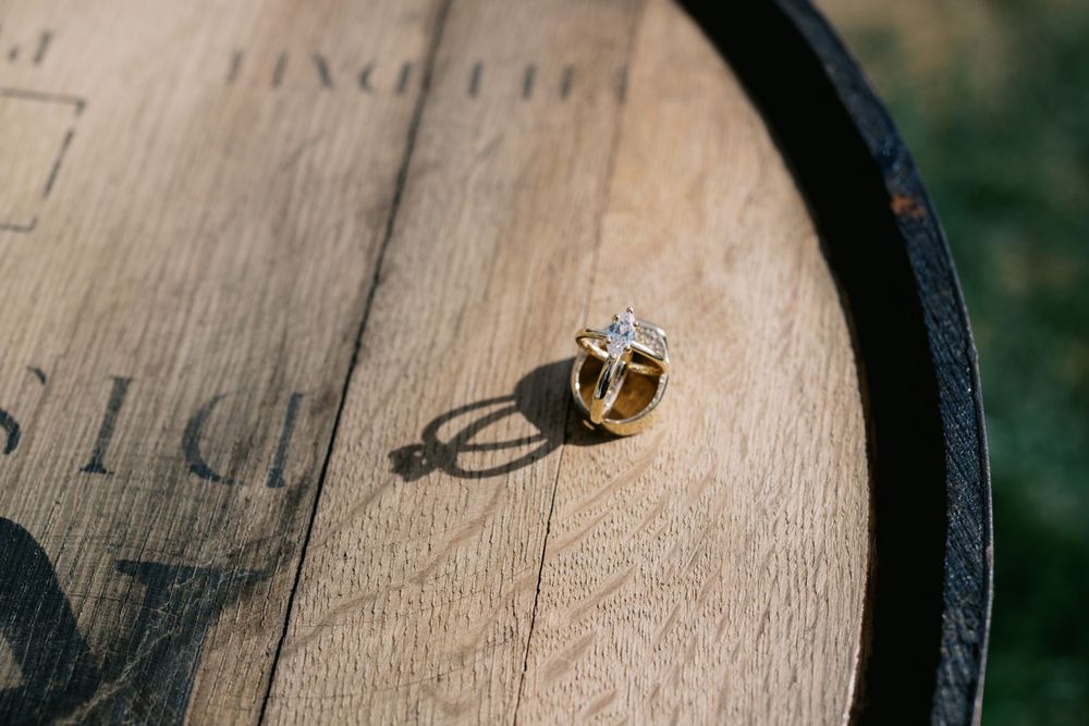 A silver and gold engagement ring casts a shadow on a wooden wine barrel surface.