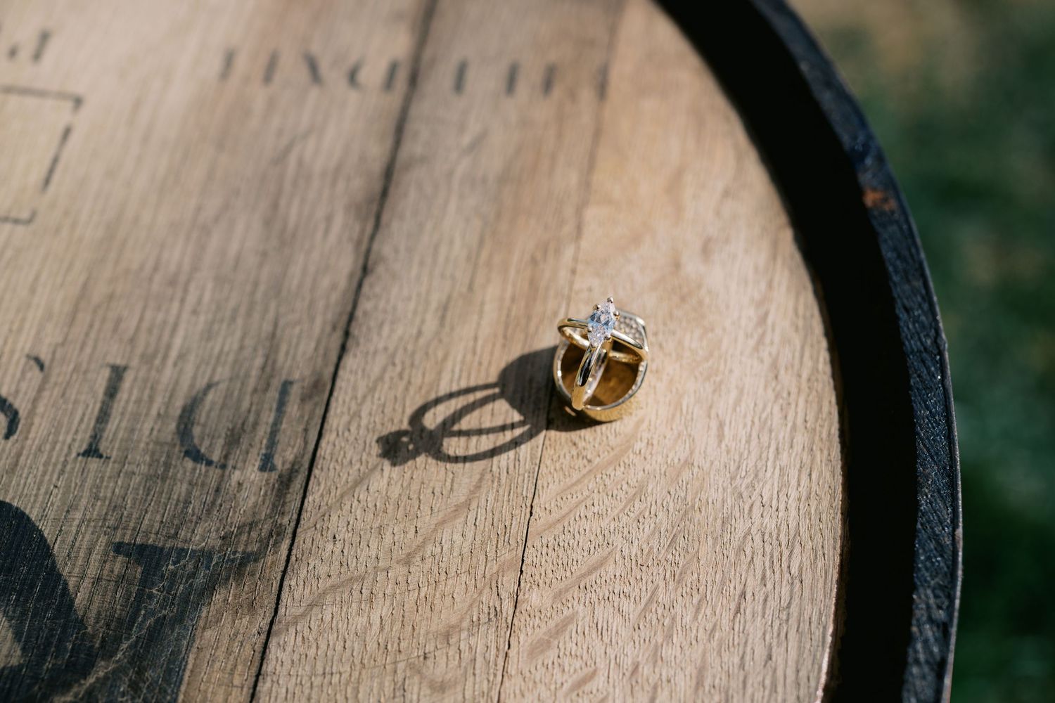A silver and gold engagement ring casts a shadow on a wooden wine barrel surface.