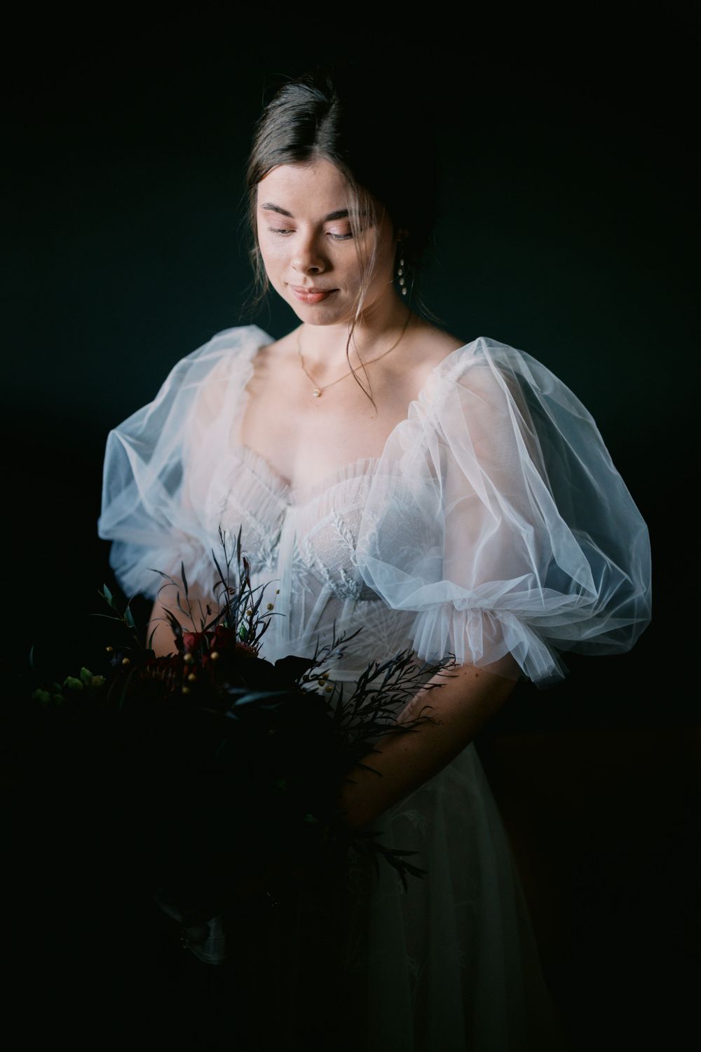 Ethereal portrait in dark setting features delicate white tulle dress with puffed sleeves and dried floral elements.