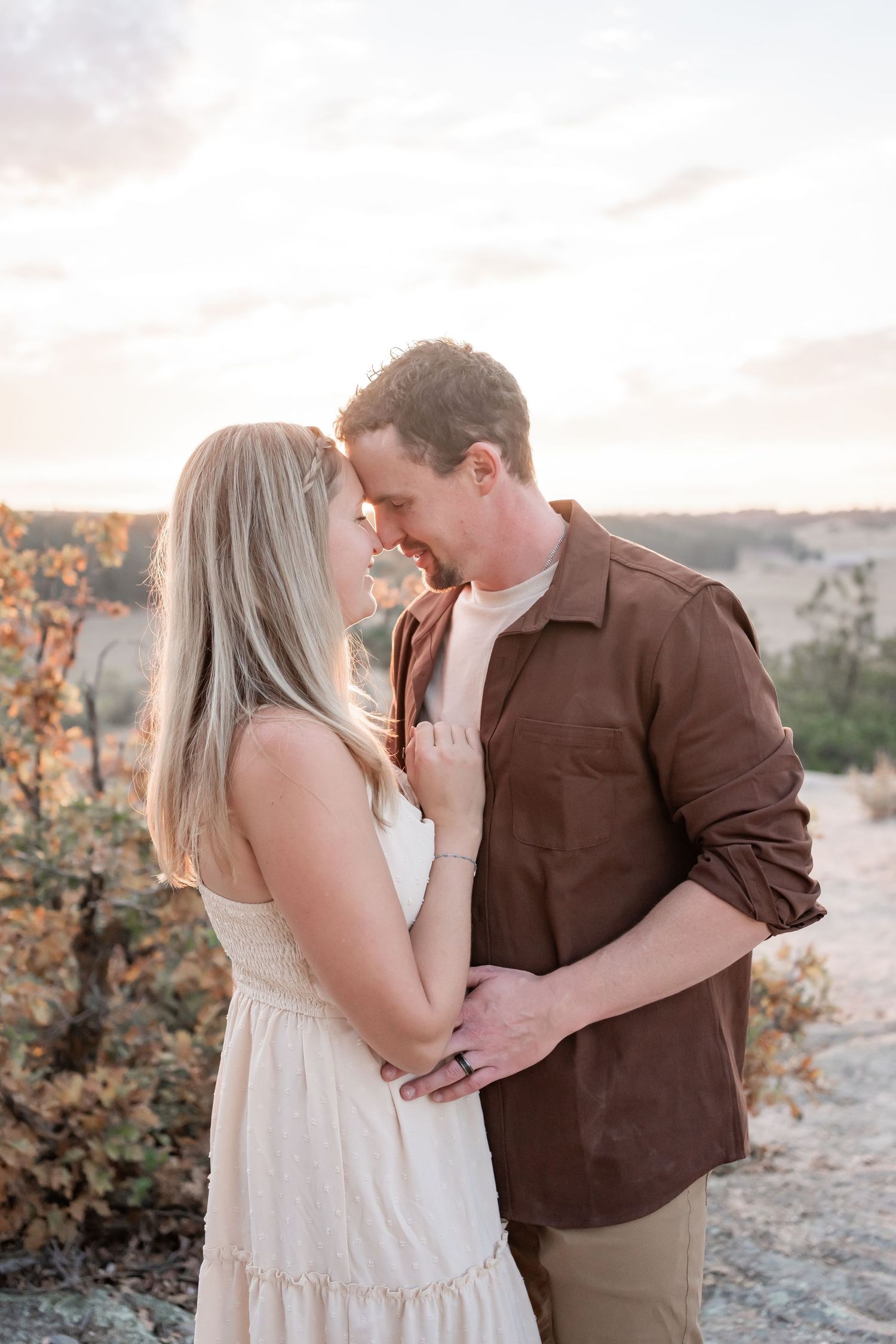 Couple shares tender moment during sunset engagement photoshoot in nature.