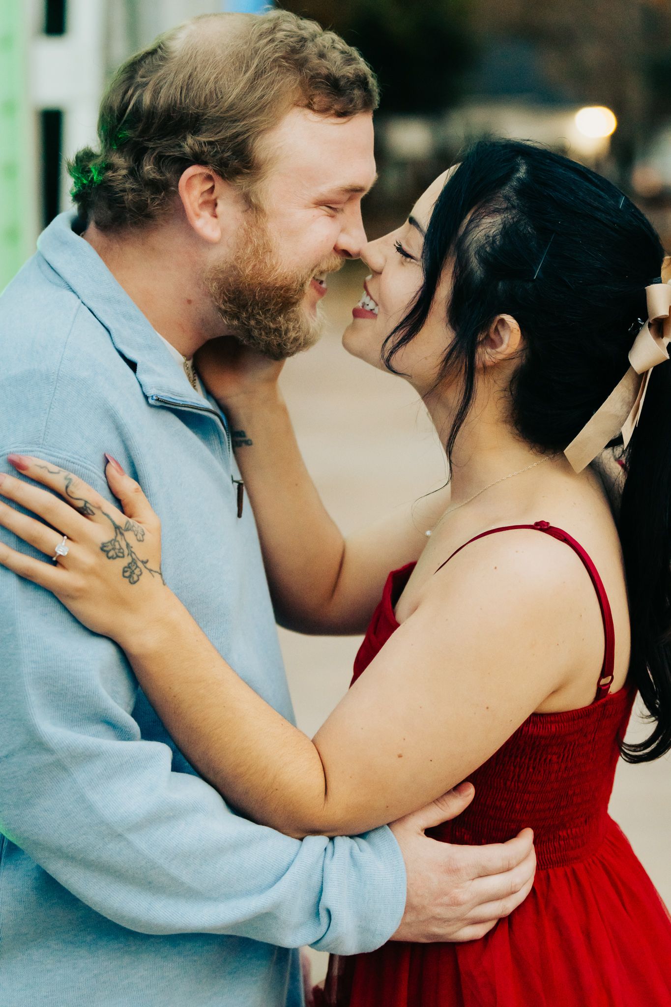 A tender embrace between two people, with one wearing a red dress and the other in light blue.