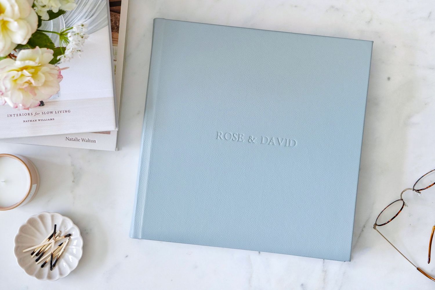 A light blue colored box surrounded by elegant white floral accents and minimalist decor on a light surface.