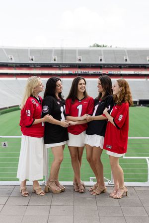 Row of graduates showing off their shoes while sitting on stadium wall.