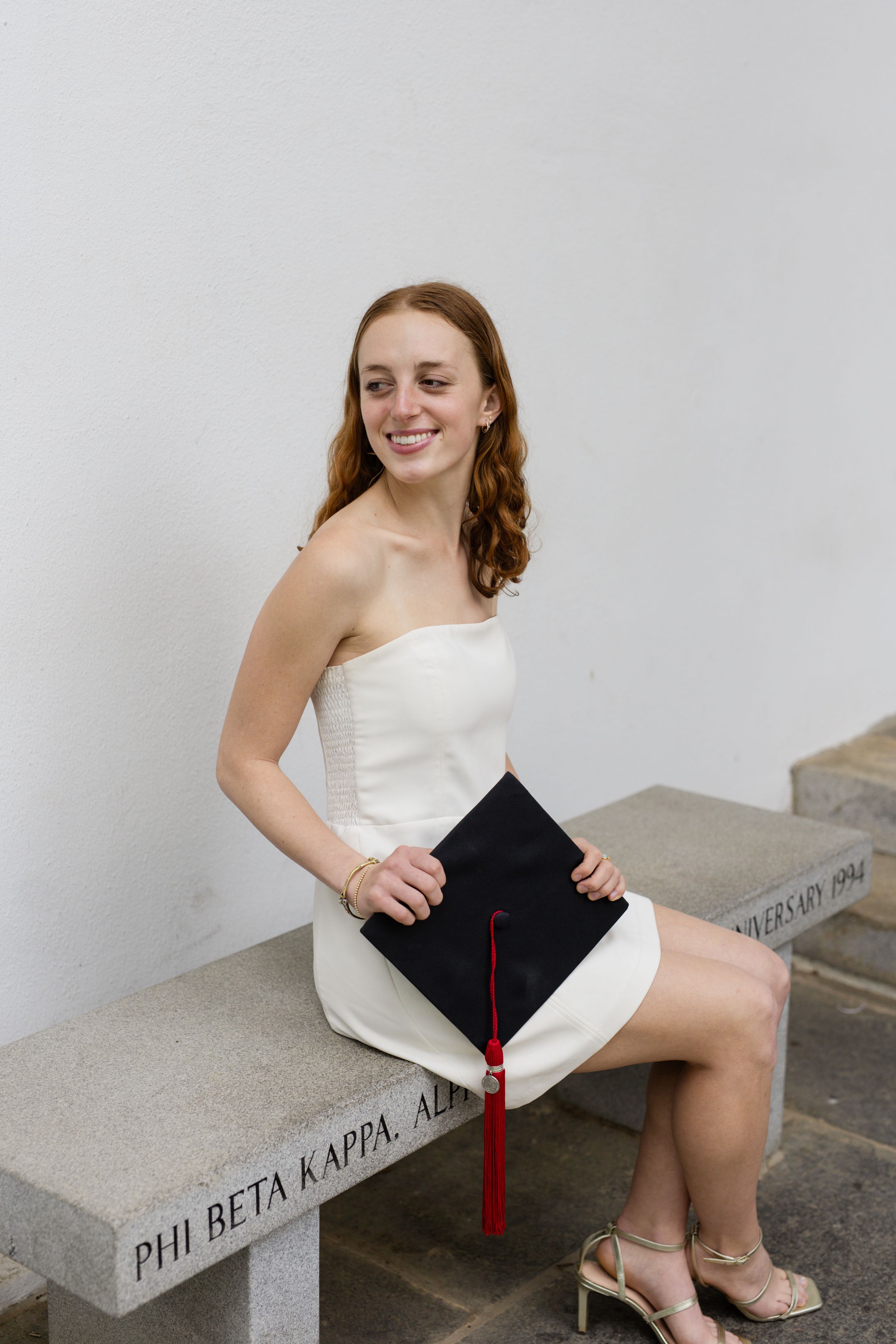 Graduate in white dress posing with cap on concrete steps.