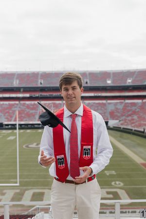 Graduate in white and red regalia posing at UGA football stadium.