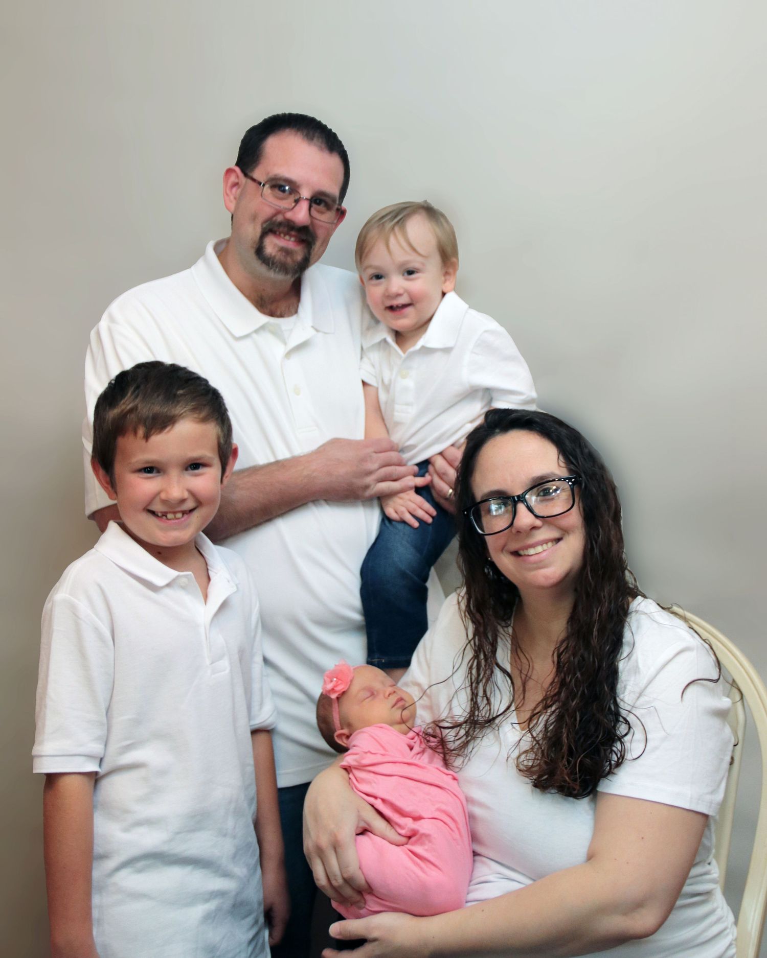 Family portrait in matching white outfits against neutral background.