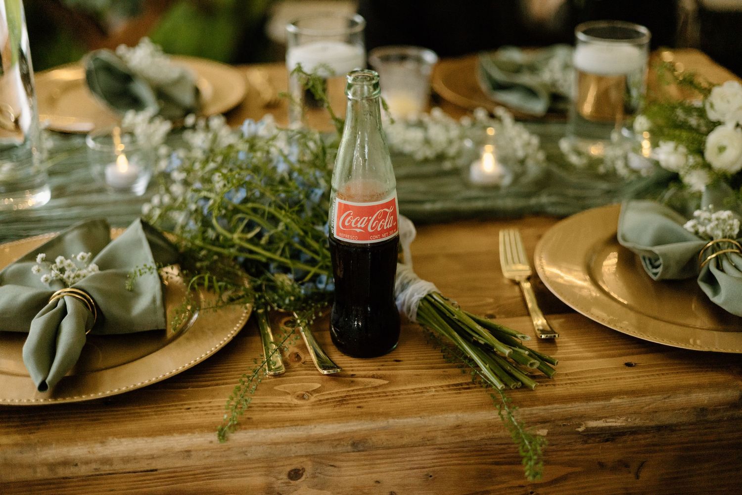 Elegant table settings with gold charger plates, eucalyptus greenery, and vintage Coca-Cola bottles for a rustic reception.
