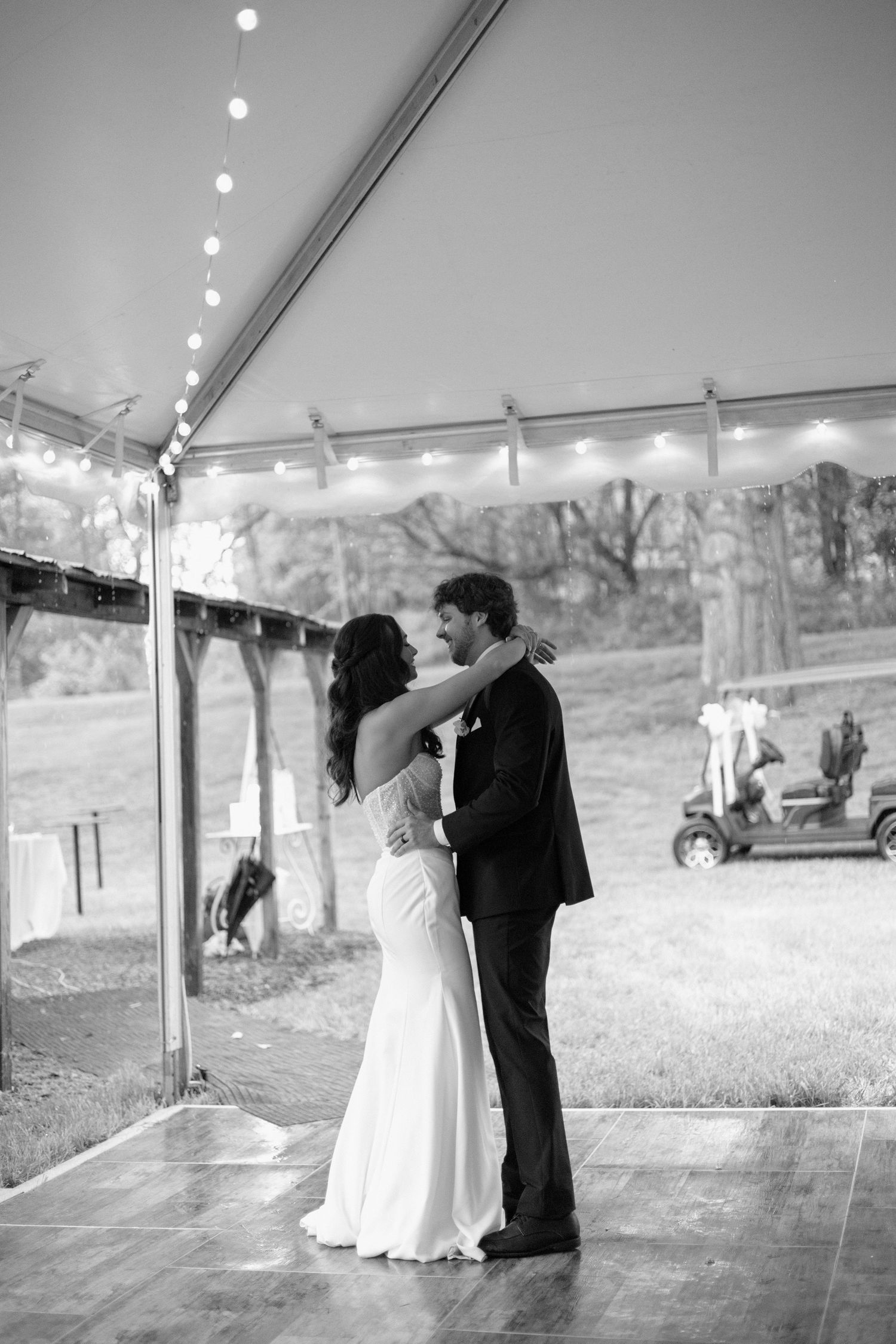 A couple shares their first dance under a tent at an outdoor wedding reception with string lights and mountain views.
