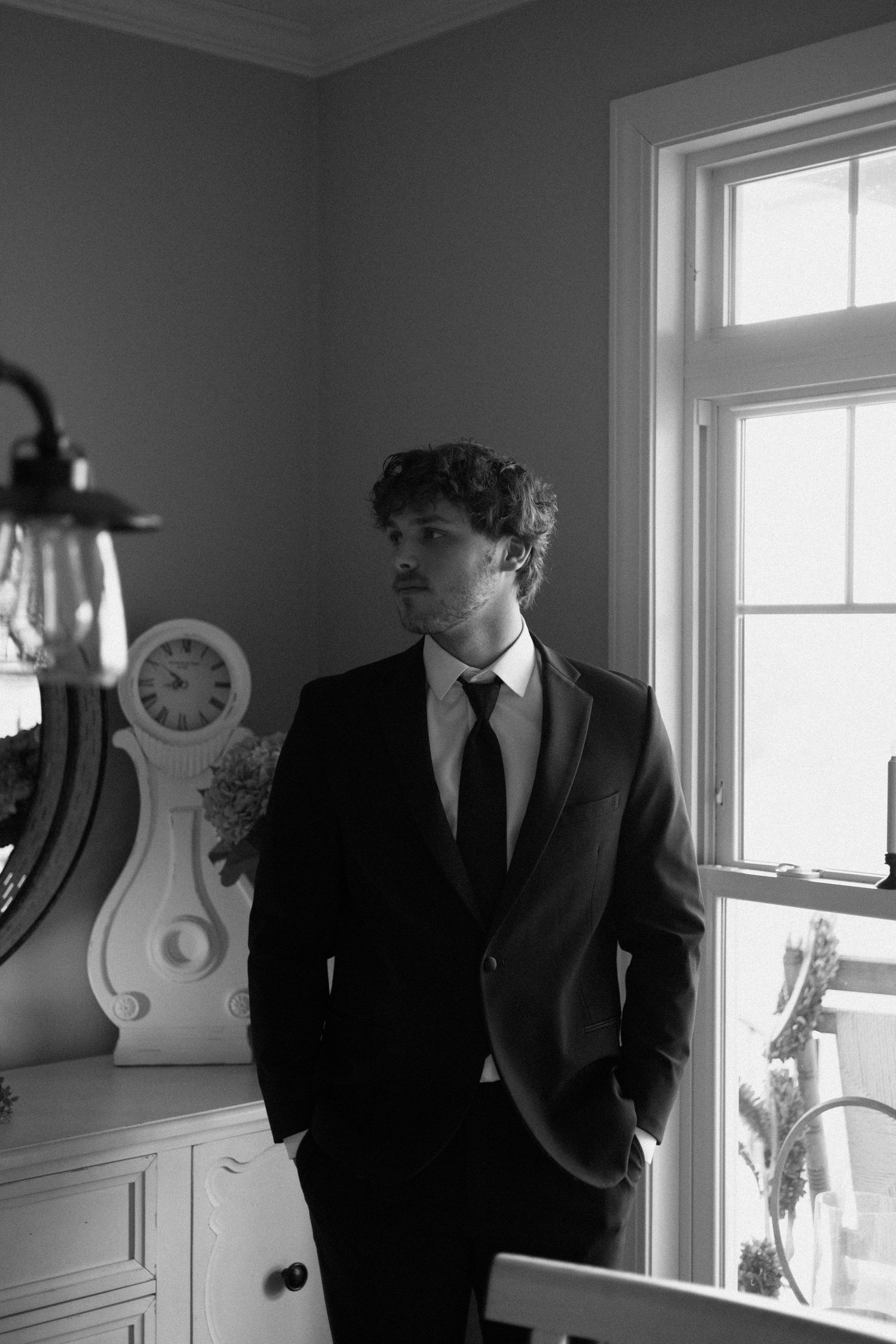 Black and white photo series showing a figure in a dark suit and hat standing by windows in an elegant interior.