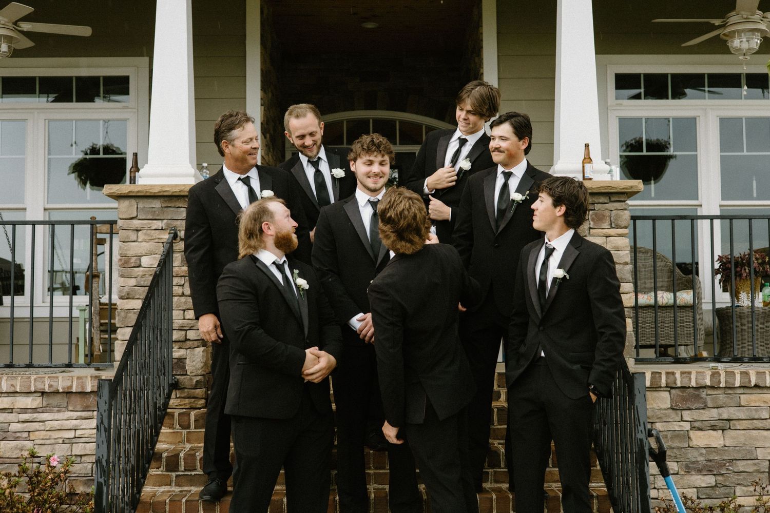 A group in formal black suits and ties stand together on stone steps of a white-columned building.