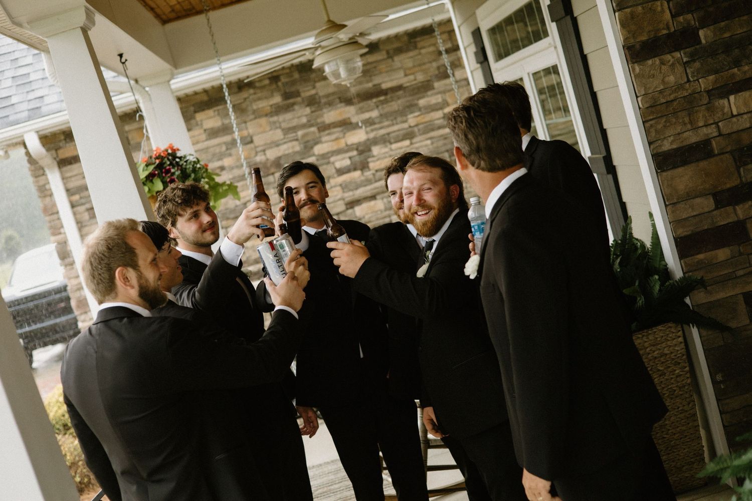 A group wearing black formal attire gathers on a covered porch, engaged in cheerful conversation.