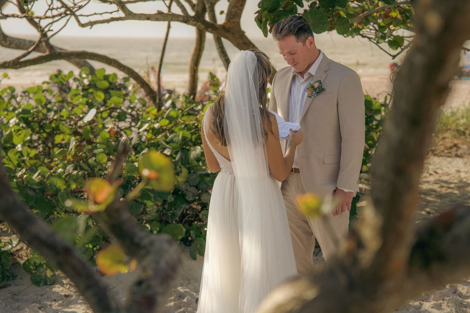 Romantic wedding couple in beige and white attire share an intimate moment among yellow flowers and greenery.