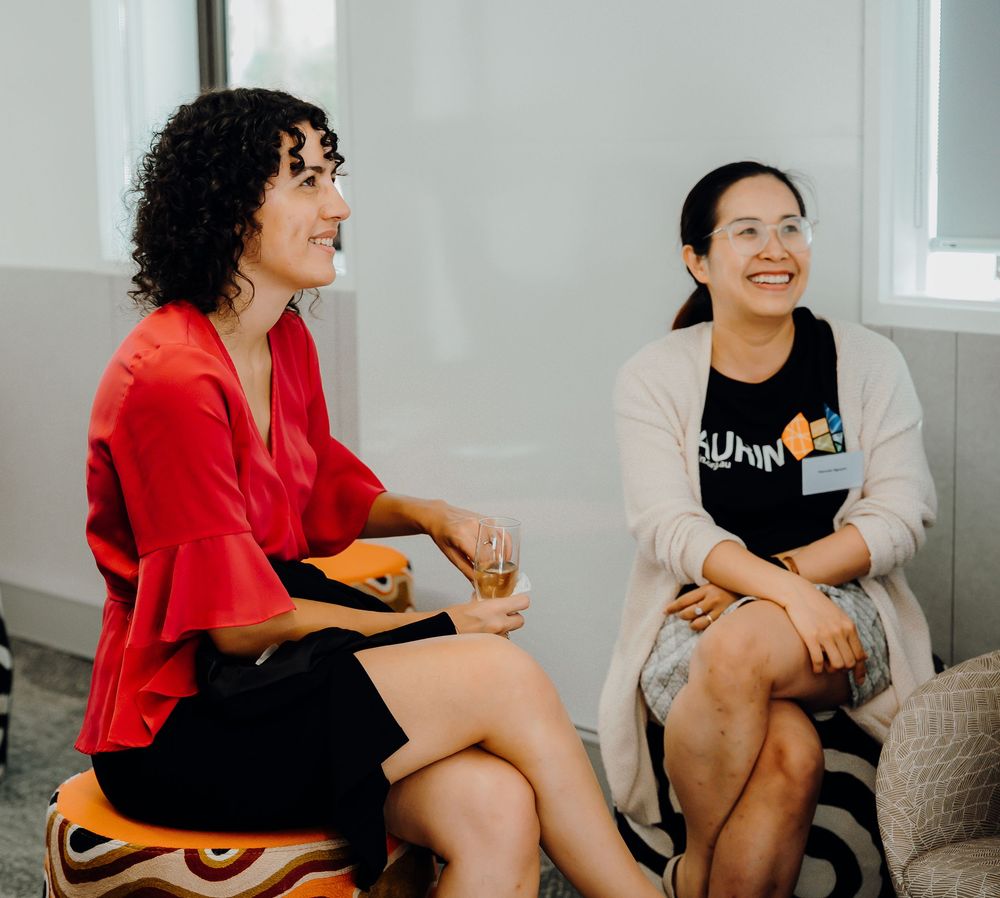 A group of friends gather around a sofa laughing and enjoying drinks in a casual setting.