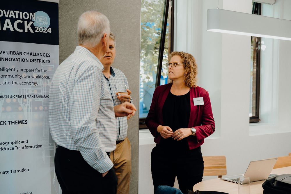 Business professionals engage in conversation at a professional networking event with presentation boards visible.