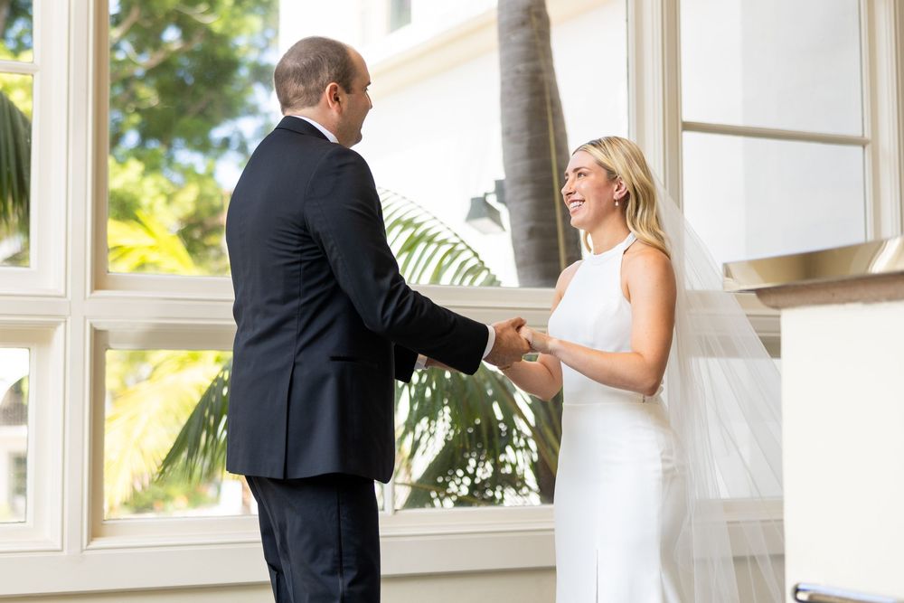 A couple in wedding attire shares a romantic first dance moment in a bright sunlit venue.
