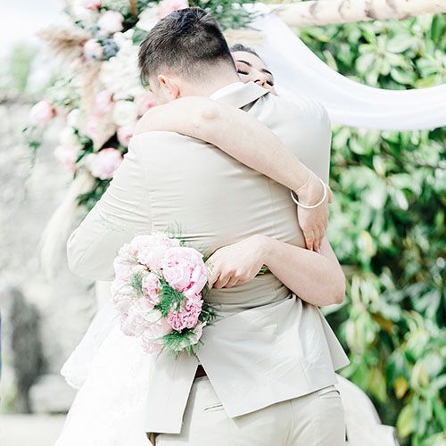 Photographe mariage fine art à Lectoure – étreinte lumineuse des mariés sous une arche fleurie aux teintes pastel - Laetitia KLOPOCKI