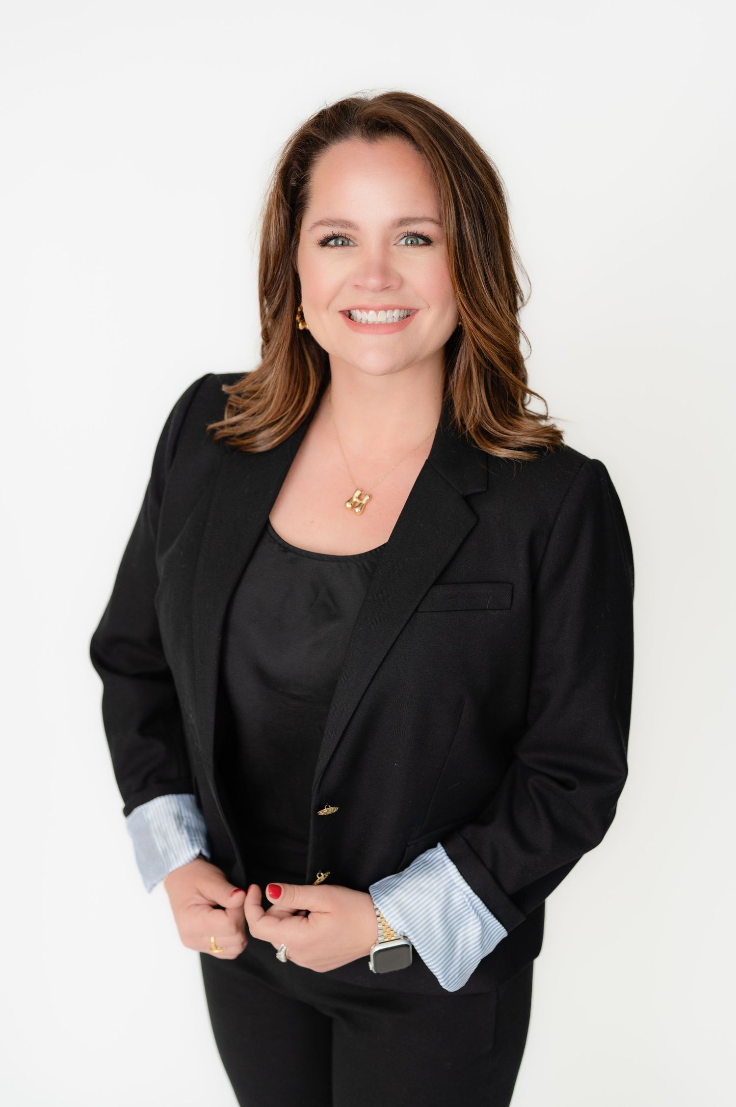 Professional in a black blazer and top poses confidently against white background while smiling warmly.