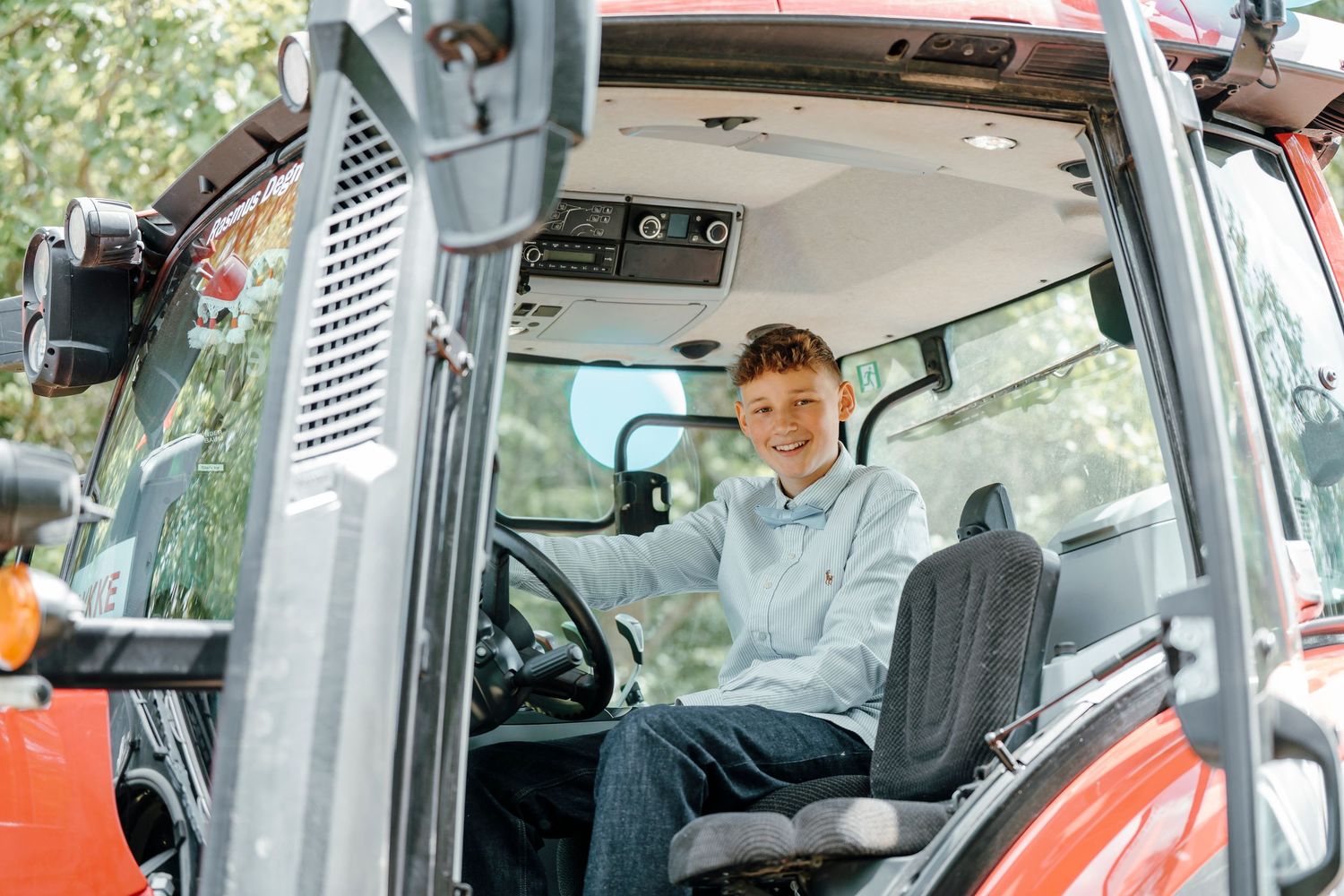 Young operator seated inside modern red tractor cab wearing blue hoodie sweatshirt during harvest season.