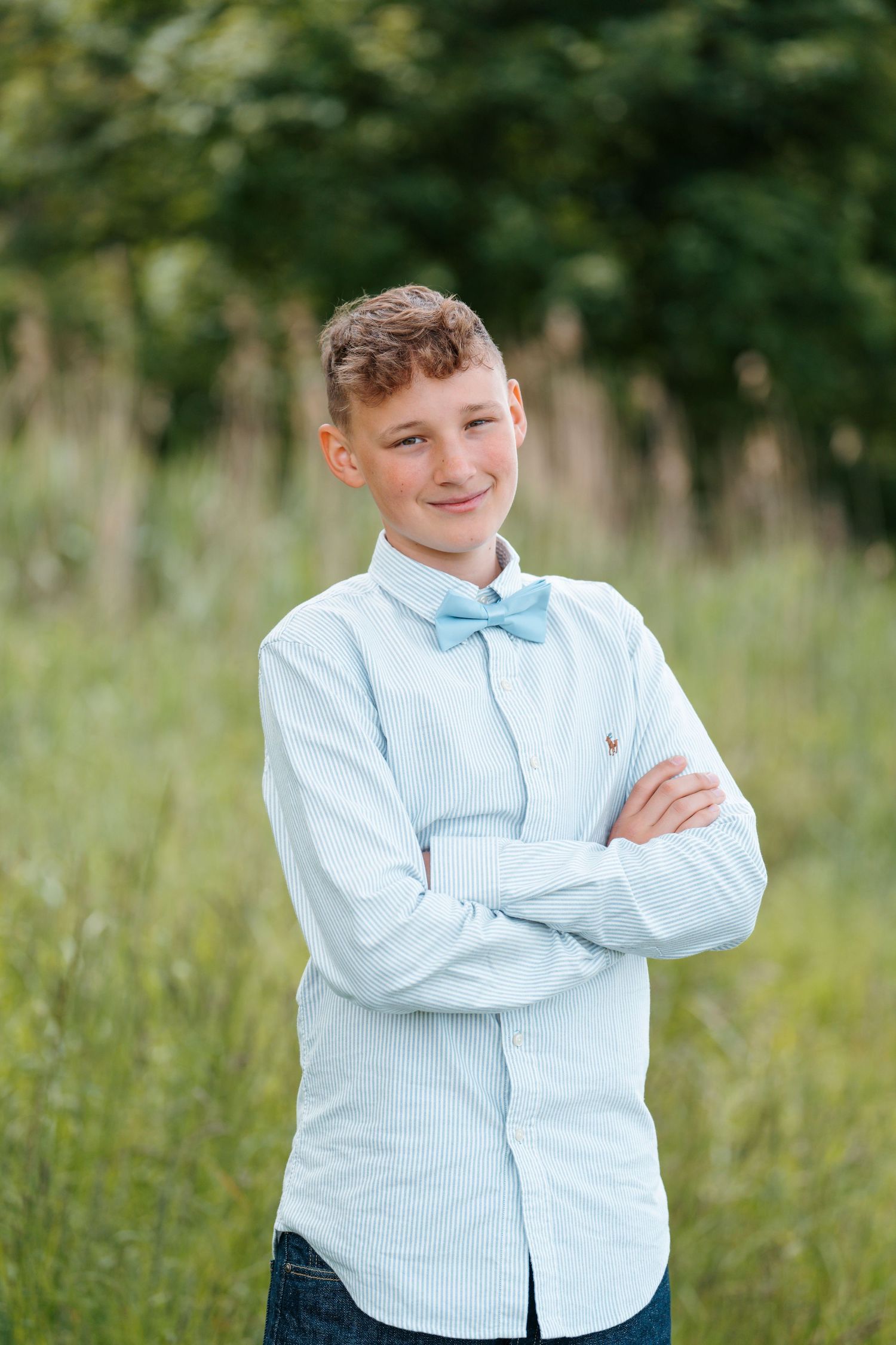 Young person in light blue button-down shirt smiling and standing outdoors in natural grassy setting.