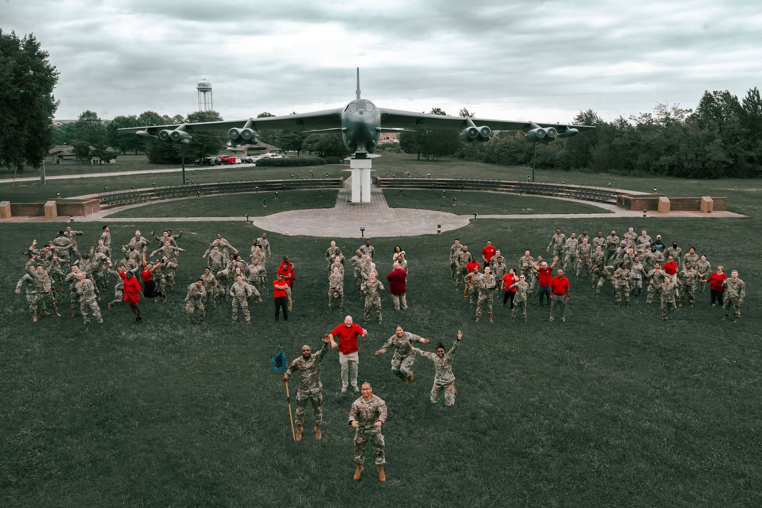 Military formation creates heart shape on green lawn with aircraft displayed in background.