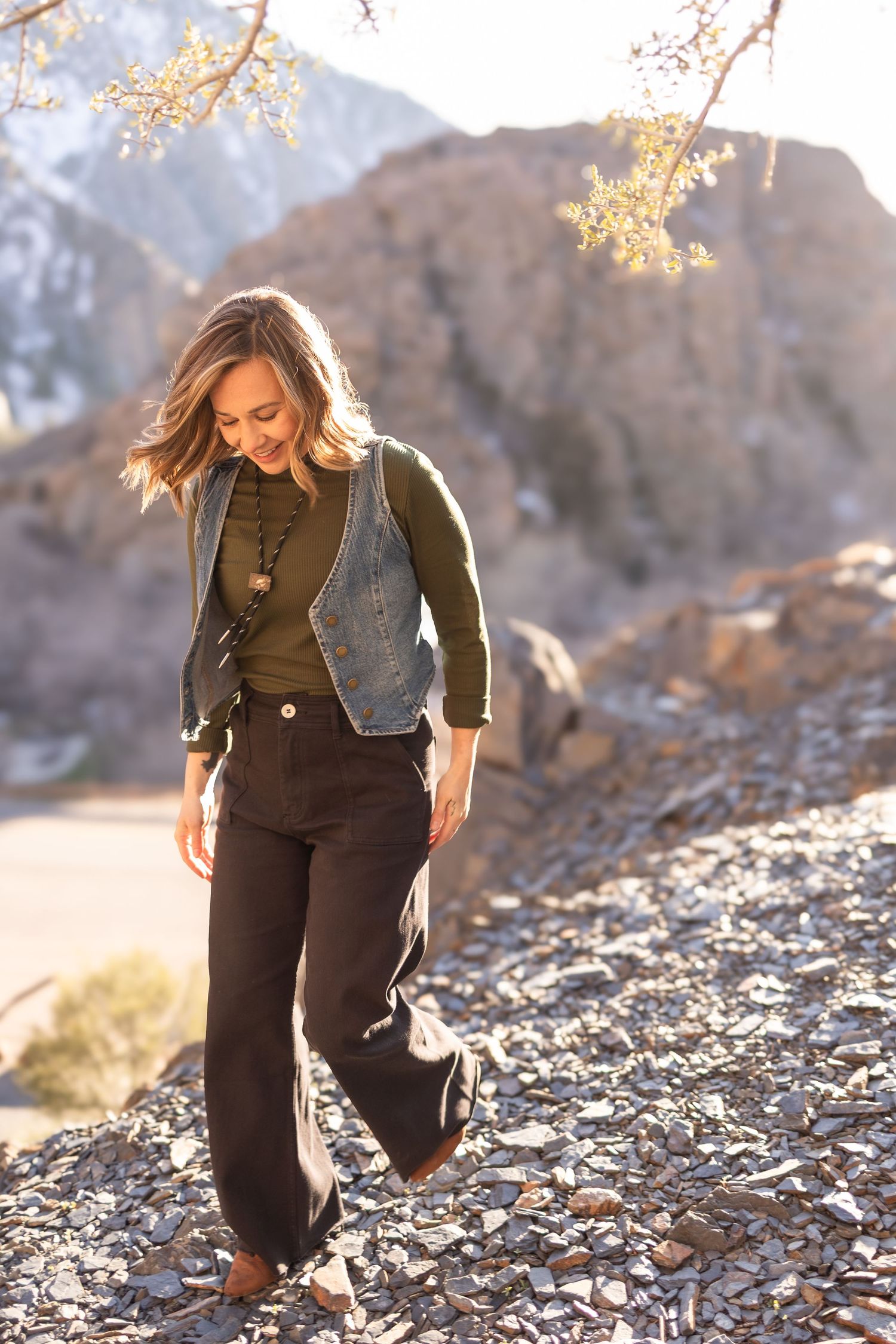 Woman poses playfully on rocky terrain at sunset with mountains in the background for master's degree graduation portraits in Utah.