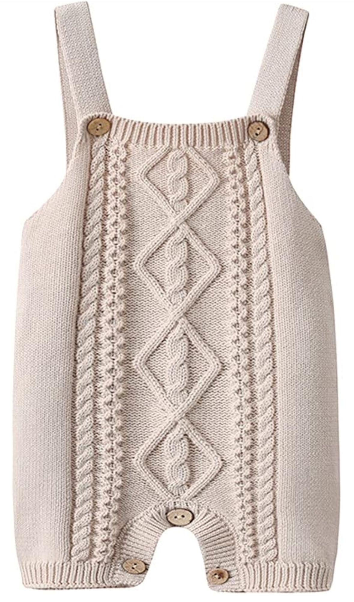 Cream-colored knit baby romper with cable pattern design and button details featuring shoulder straps.