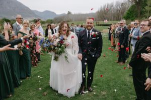Guests throw flower petals at outdoor wedding ceremony in front of mountain landscape.