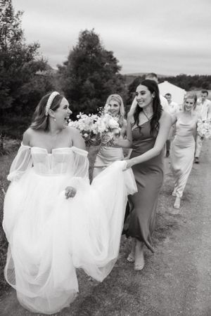 Candid moment of bridesmaids helping with the bride's dress while walking outdoors.