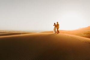 Silhouetted couple stands together on sand dunes during golden sunset.