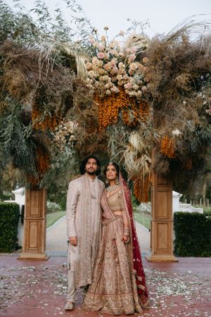 Wedding arch decorated with dried flowers and orange accents against outdoor backdrop.