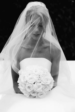 Black and white wedding photo with a bride in a strapless gown holding a white rose bouquet beneath a flowing veil.