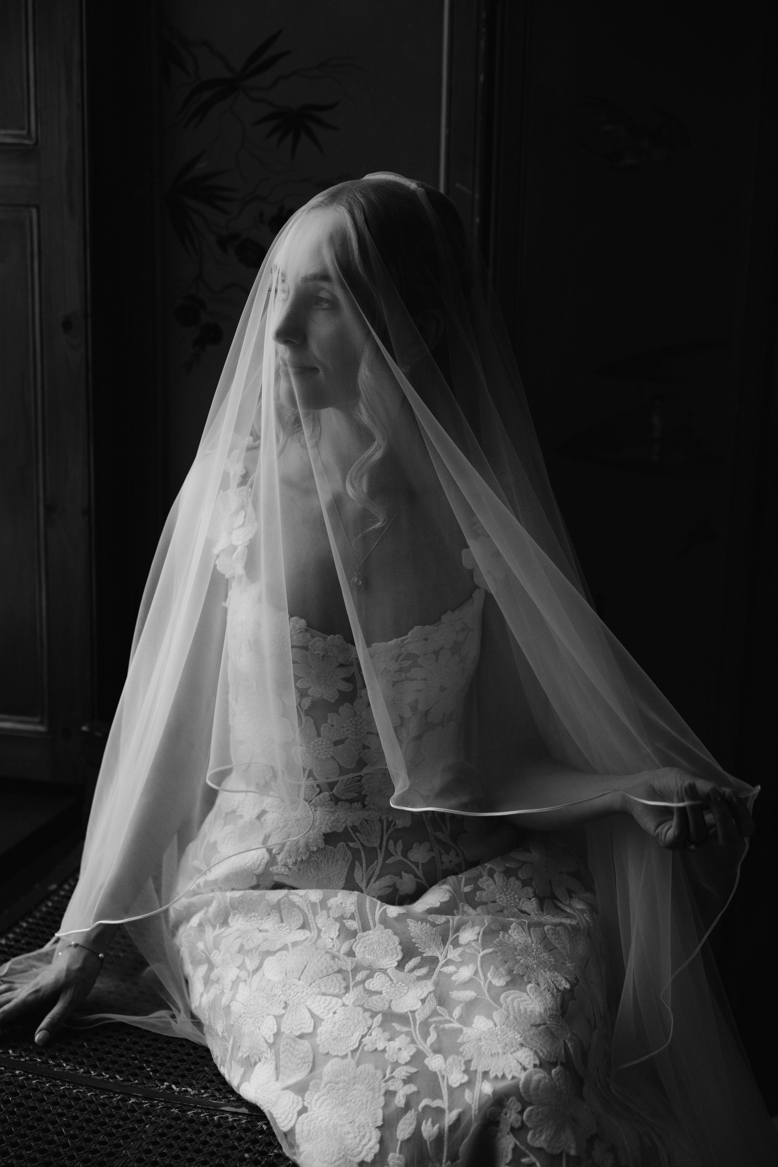 Artistic black and white photo of a bride wearing a delicate veil in dramatic lighting.