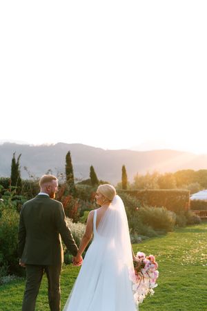 A couple admires the Tuscan sunset landscape on their wedding day from a hilltop garden surrounded by cypress trees.