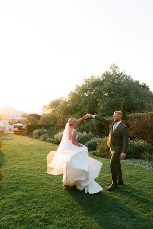 Two figures dancing on a grassy lawn at sunset, with white wedding dress flowing in the golden light.