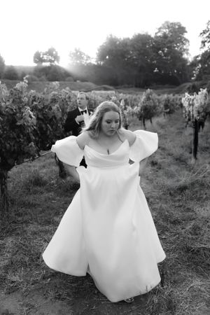 A black and white photo of a flowing white wedding dress in a vineyard setting at sunset.