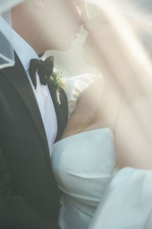 Soft-focused romantic wedding photograph showing black tuxedo with bowtie and white bridal gown in ethereal lighting.
