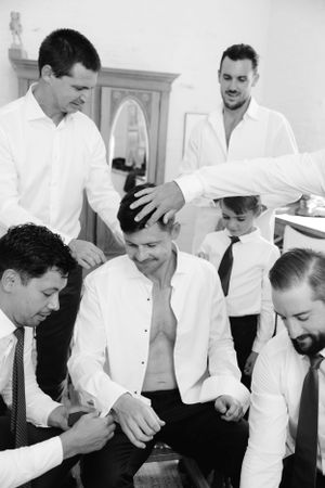Groomsmen in white shirts help prepare for a wedding in black and white vintage style photograph.