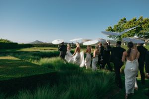 A wedding party walks along a grassy hill under a bright blue sky at an outdoor venue.