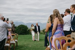 Wedding ceremony with guests watching couple walk down aisle with mountains in background.