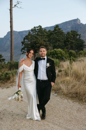 Elegant wedding couple walking on a path with mountains in the background.