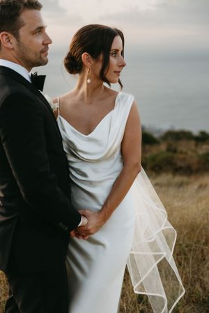 Elegant couple poses for a romantic wedding portrait at dusk in formal attire.