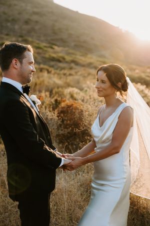 Sunset wedding portrait with couple holding hands against mountain backdrop.