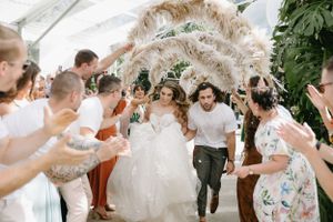 Wedding exit celebration with pampas grass and cheering guests in white tent.