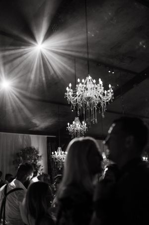 Elegant crystal chandeliers illuminate a dark reception space with silhouettes of guests below.