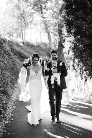 Black and white photo of newlyweds walking down a tree-lined path.